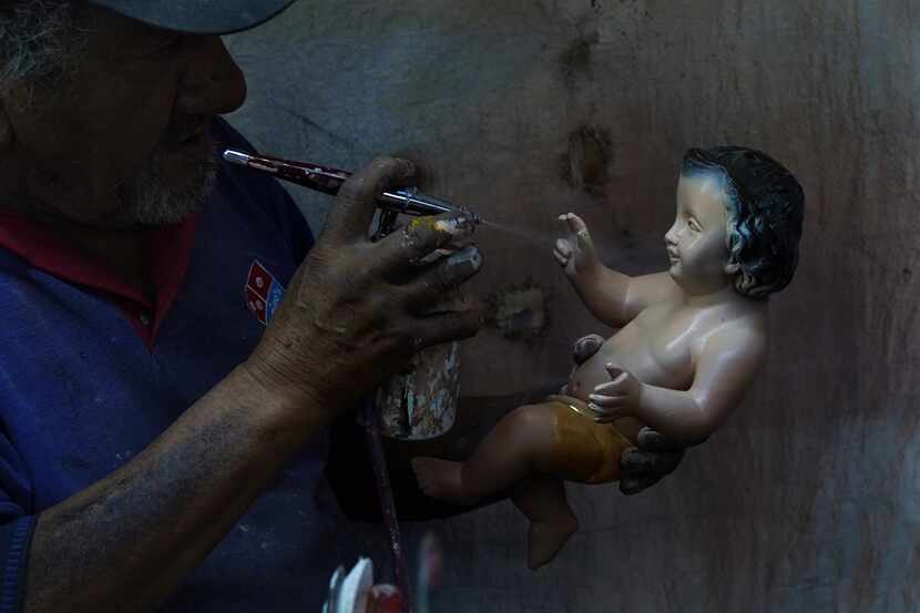 Un hombre pinta una figura del niño Dios restaurada en preparación para la fiesta del "Día...