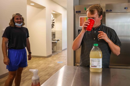 Caretaker Tanner Ledet (left) observes 29 Acres resident Jon Heighten drinking a cup of...