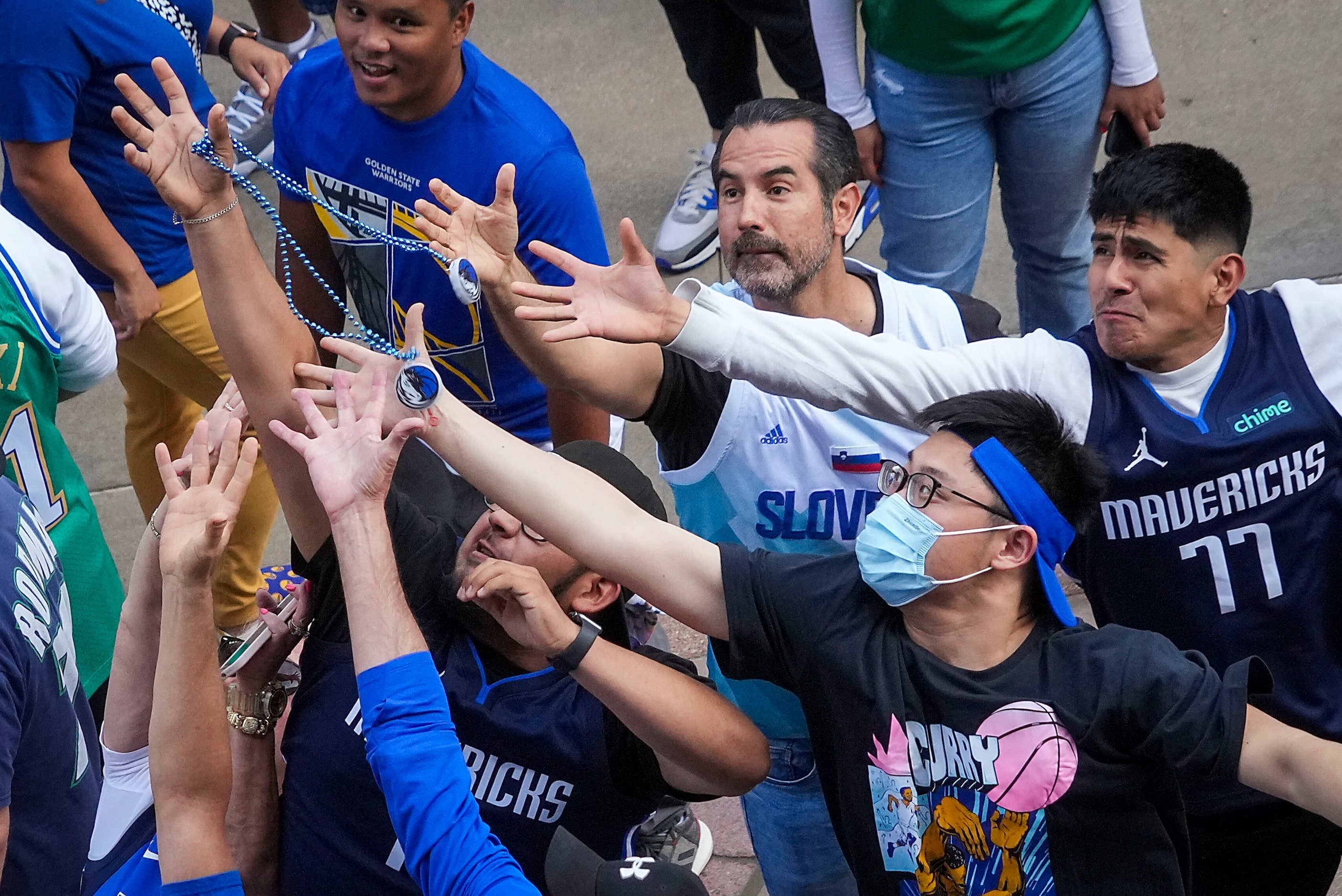 Dallas Mavericks fans reach for beads tossed to the crowd on the plaza before Game 3 of the...