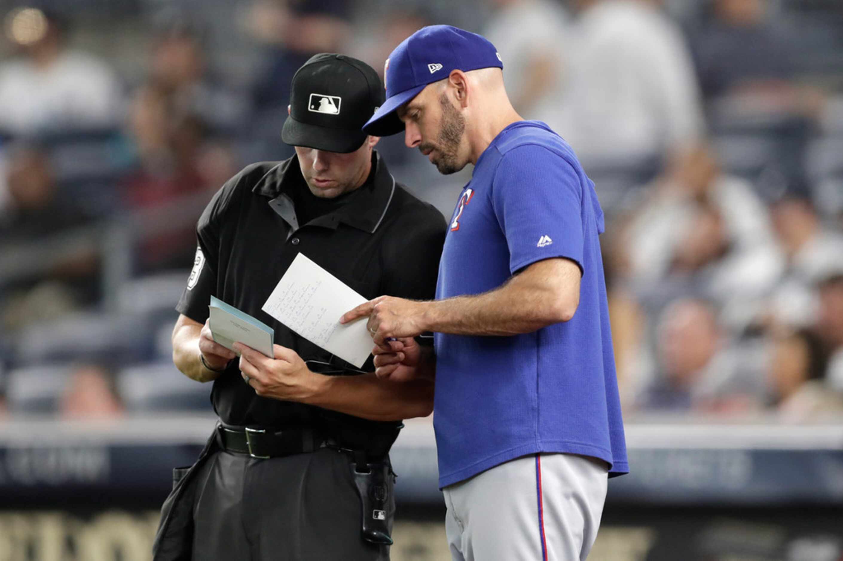 Texas Rangers manager Chris Woodward discusses lineup changes with home plate umpire Will...