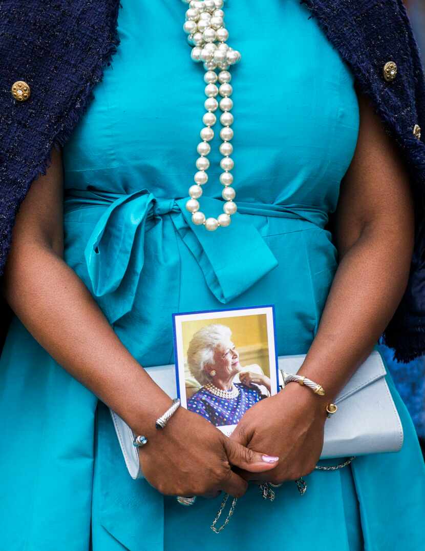 A woman wears pearls and carries a photo of Barbara Bush as she and other guests leave after...