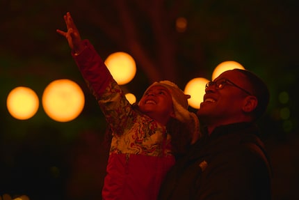 A man holds a toddler in his arms who is reaching up toward lights.