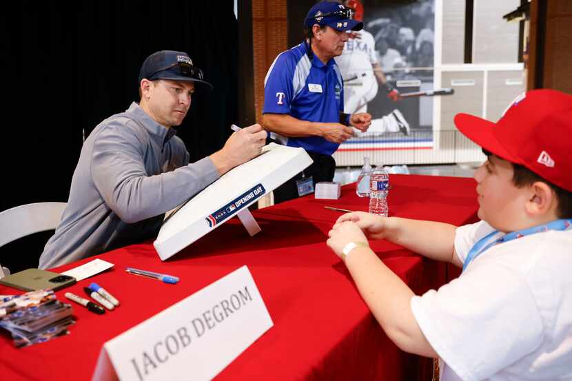 Texas Rangers’ Jacob DeGrom signs an autograph on a baseball base belonging to Andrew Long,...
