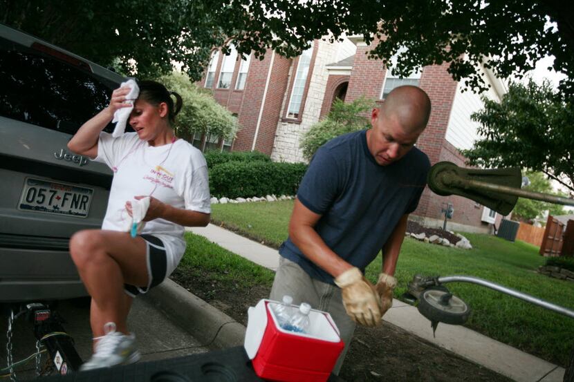 Marie Heil wipes away sweat as her husband, Aaron, gets water after the pair mowed a...
