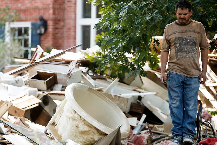 A worker stands amidst a pile of rubble in front of a house damaged by flooding from...