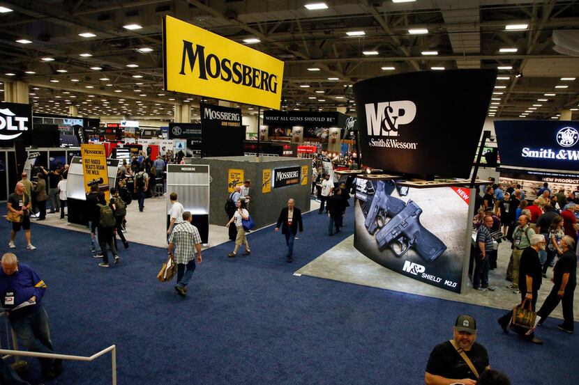 National Rifle Association convention goers walk by displays on the exhibit floor inside the...