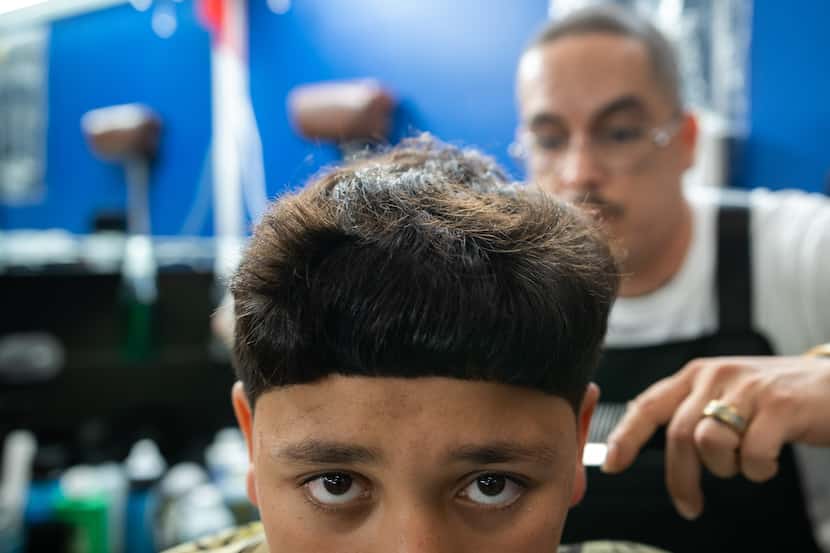 El barbero Edgar "E" Montelongo, de 35 años, corta el cabello de Nathan Cabrera, de 12,...