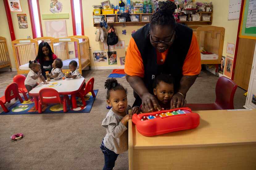 Sheree Hunter shows Zion Cooper, 1, how to play the toy piano as Ka’Maiya Terrell, 1,...