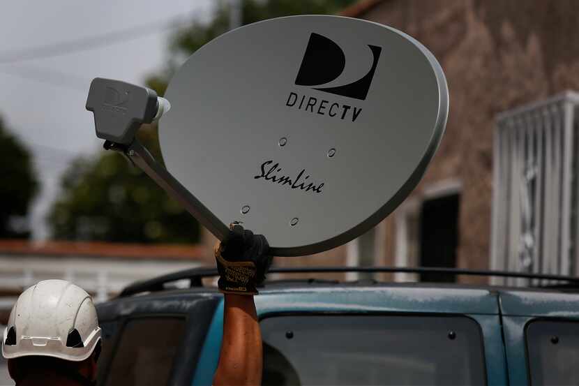 A DirecTV technician carries a new satellite TV dish while performing a new installation for...
