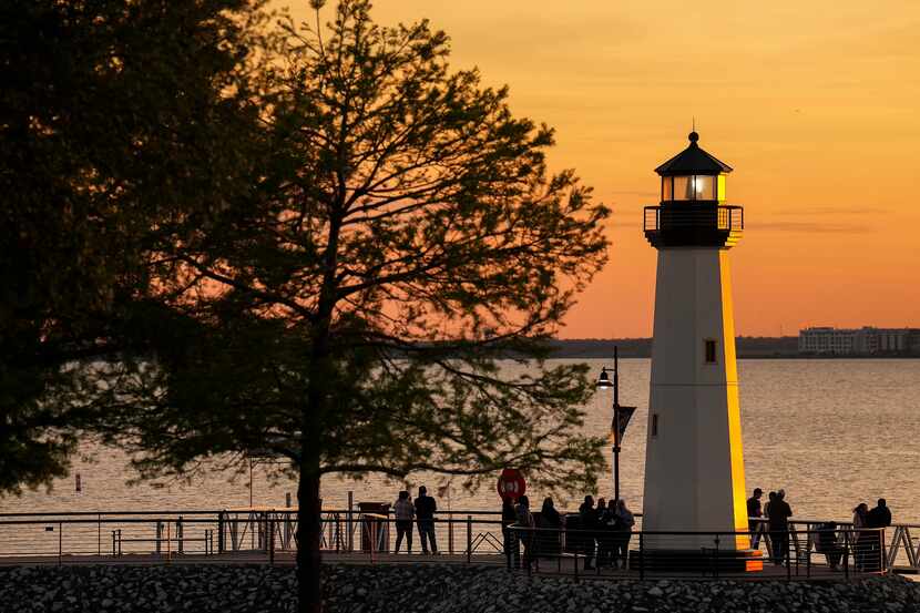 The sun sets over Lake Ray Hubbard as people visit the lighthouse at The Harbor Rockwall on...