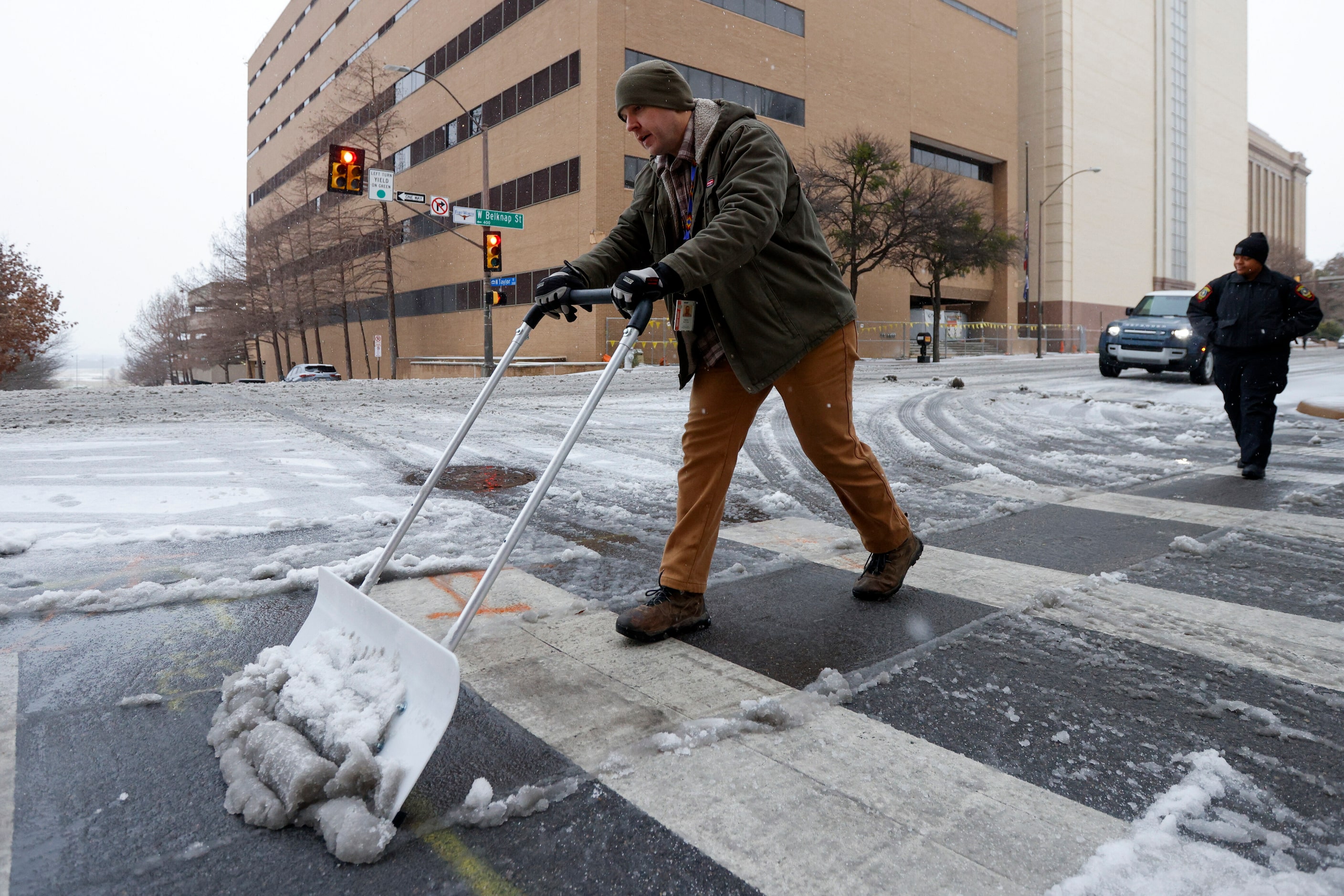 Derek Sutter, building manager for Tarrant County, shovels sleet and ice from a sidewalk on...