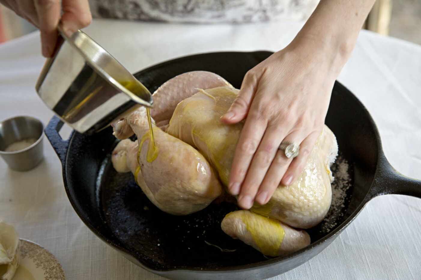 Rebecca White pours olive oil over a whole chicken before roasting it at her home Thursday,...