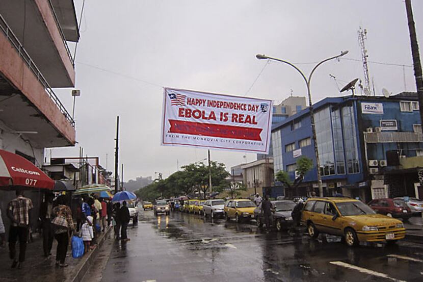 Residents of Monrova, Liberia, pass along a street under a banner warning of the threat...