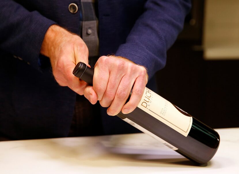 James Tidwell holds the wine bottle steady as he demonstrates how to remove the foil.