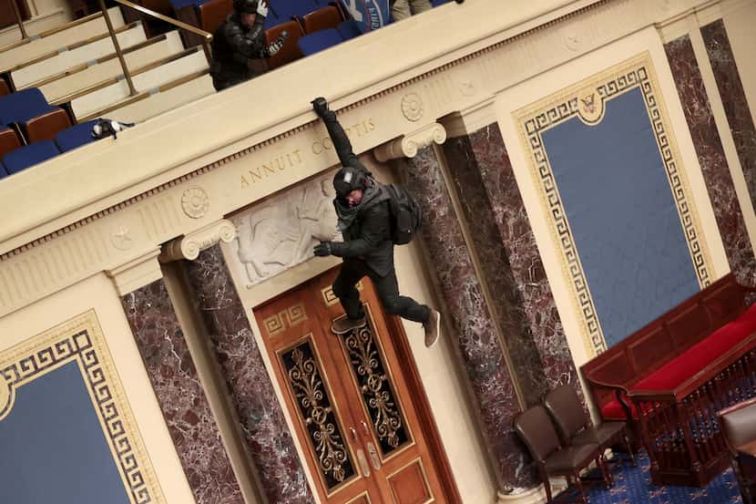 A protester hangs from the balcony in the Senate Chamber on January 6, 2021, as a mob...