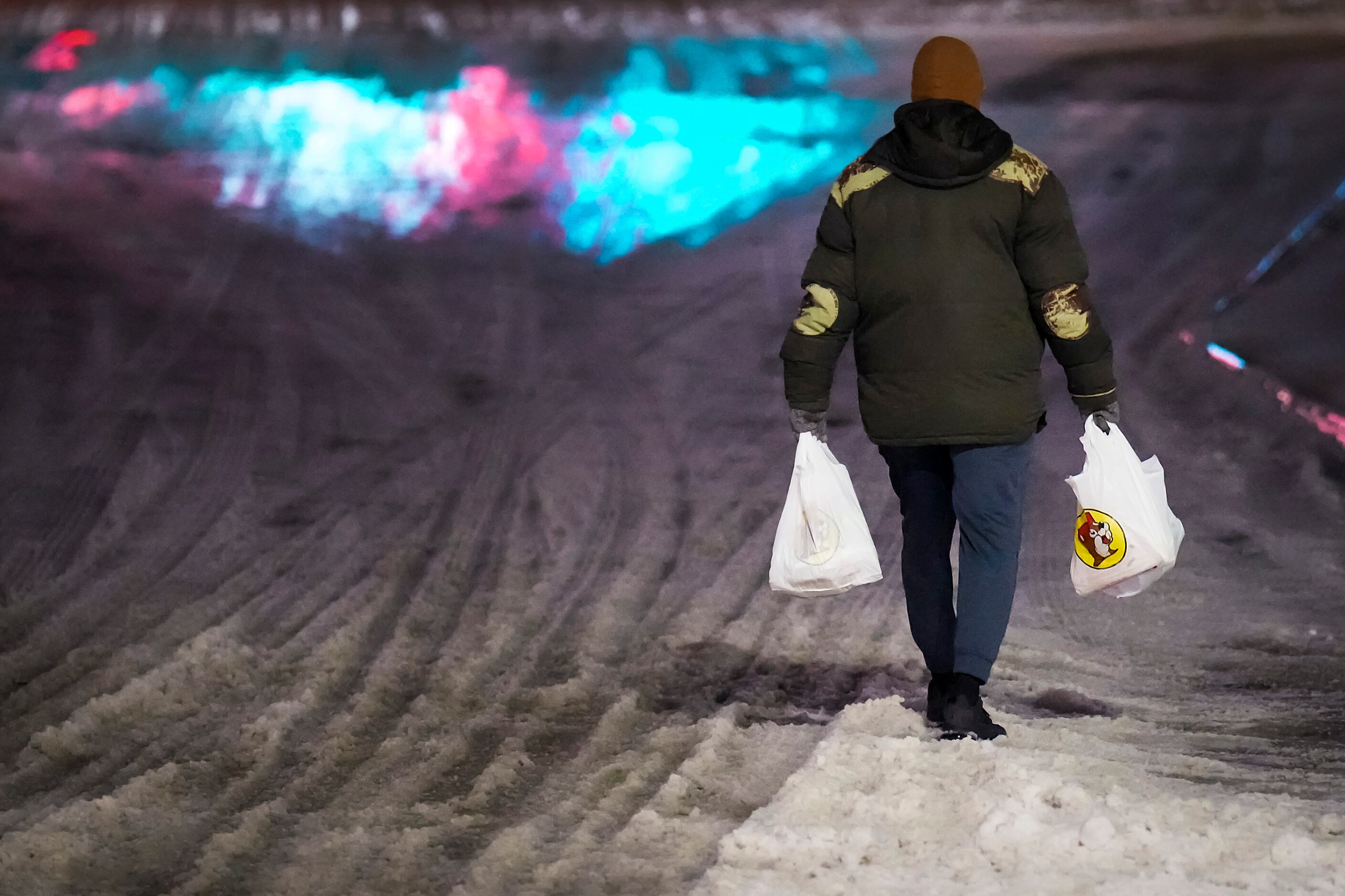 A customer carries bags through snow and ice as he walks away after making a purchase at...