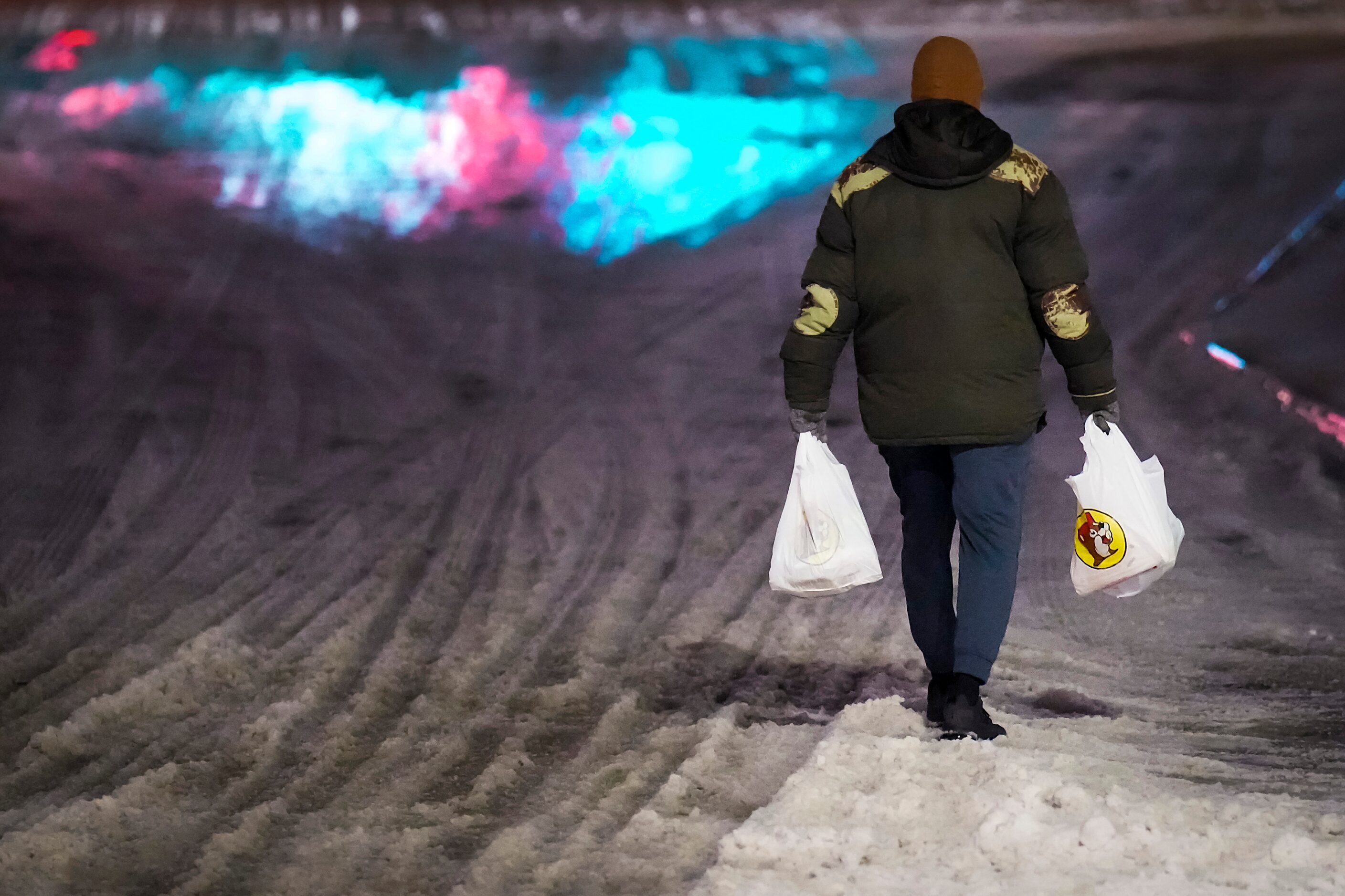 A customer carries bags through snow and ice as he walks away after making a purchase at...