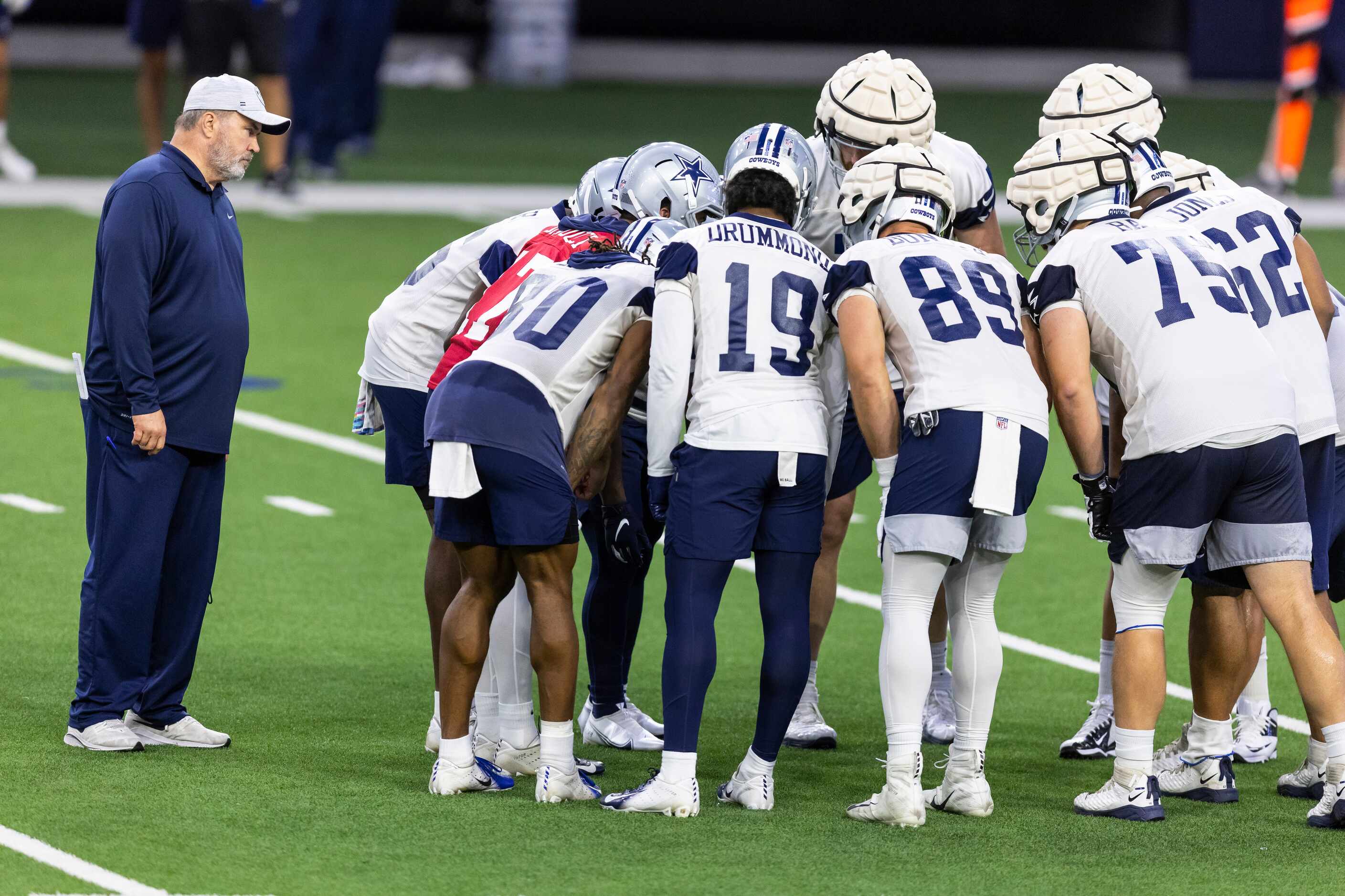 Dallas Cowboys head coach Mike McCarthy, left, looks on as offenisve players huddle during a...