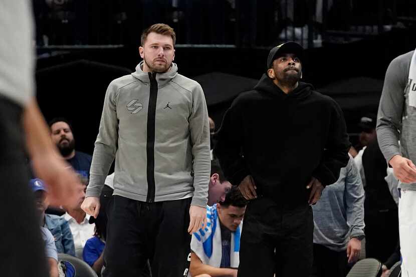 Dallas Mavericks' Luka Doncic, left, and Kyrie Irving look on from the sideline during the...