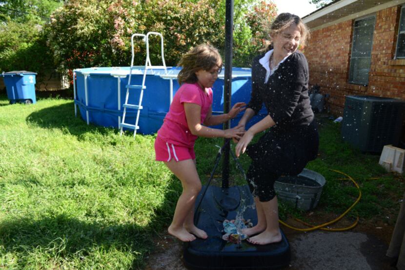 Sisters Zadie (left) and Zoe Wittrock splash water from the base of a basketball goal in the...