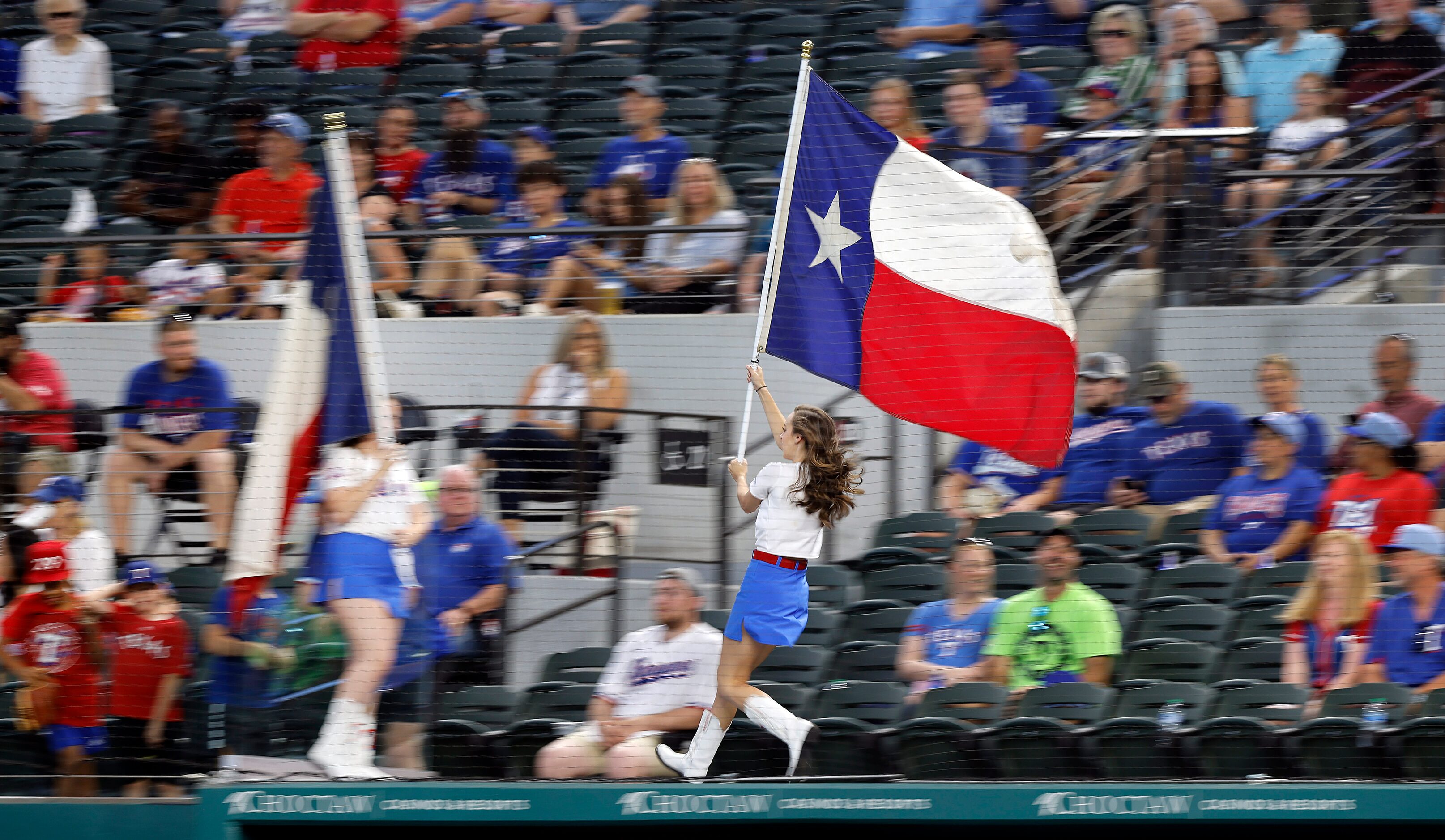 Members of the Texas Rangers Six Shooters race across the dugout with the Texas flag during...