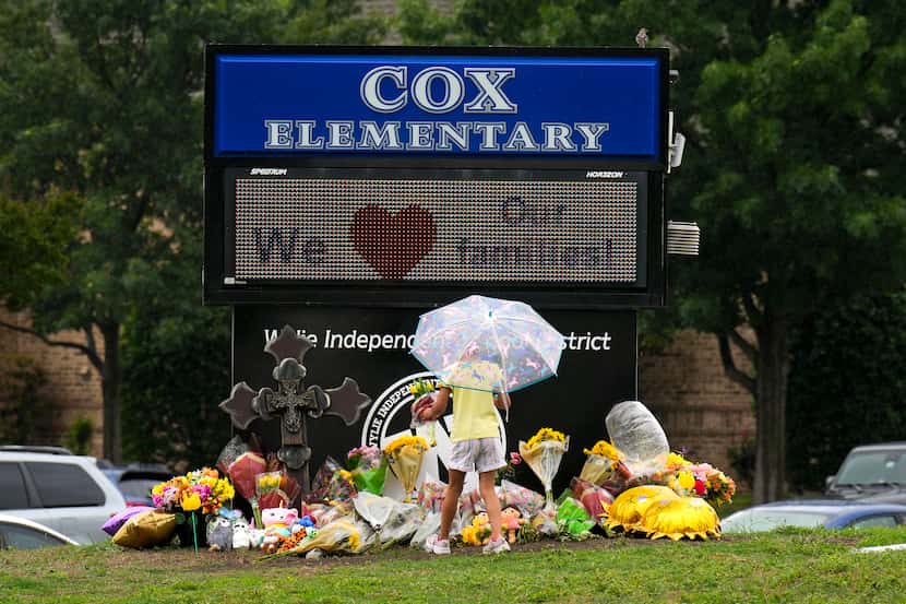 A child placed flowers on a memorial to Daniela and Sofia Mendoza at Cox Elementary after...