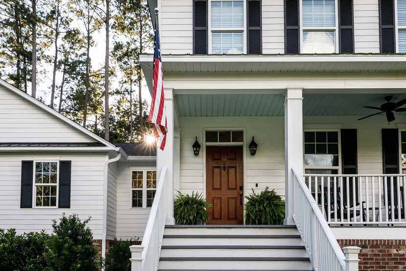 The front of a white, two-story home with an American flag hung on the porch.