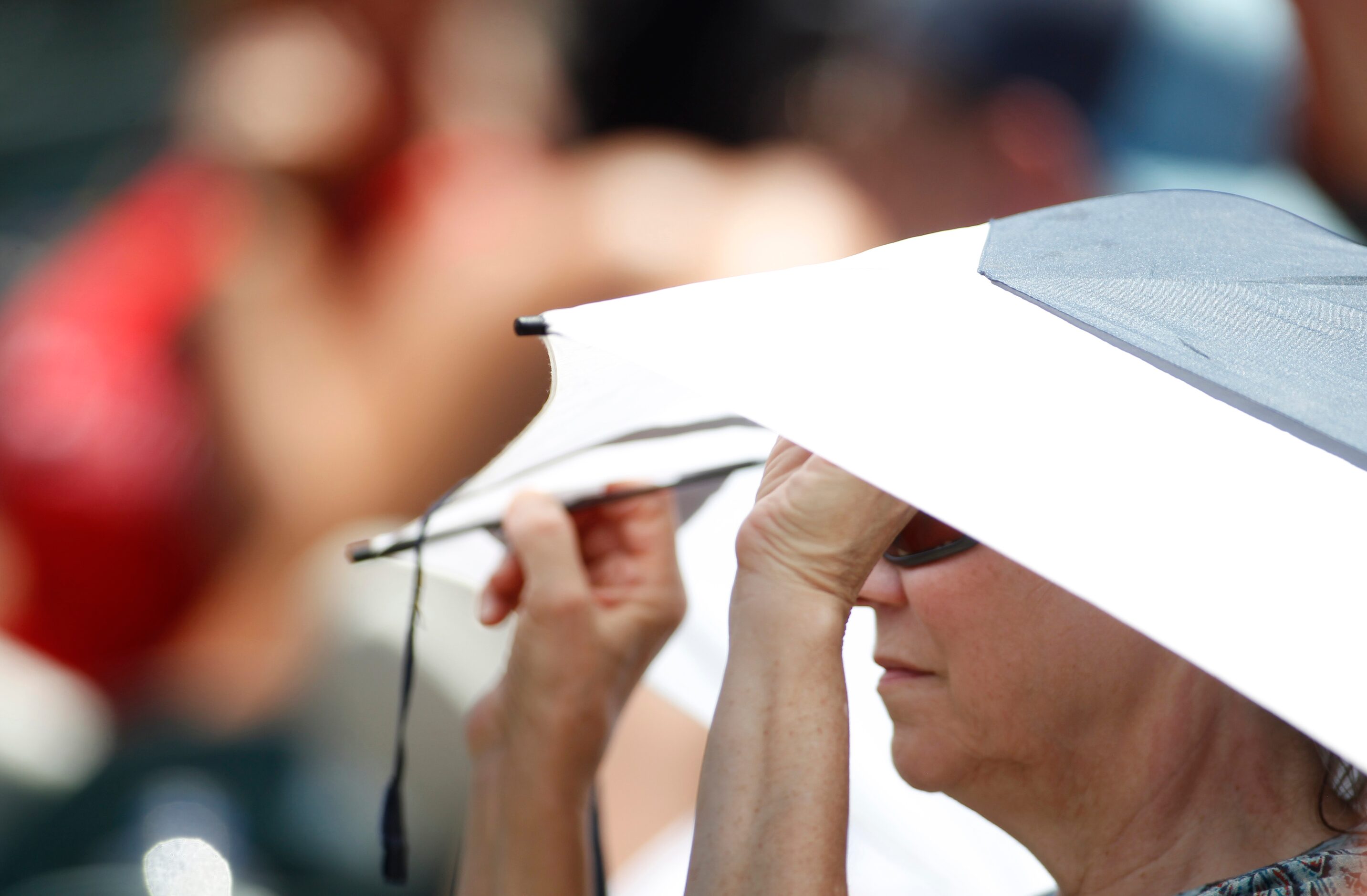 A fan uses an umbrella for relief from the sun during the 4th inning of the Rockwall versus...