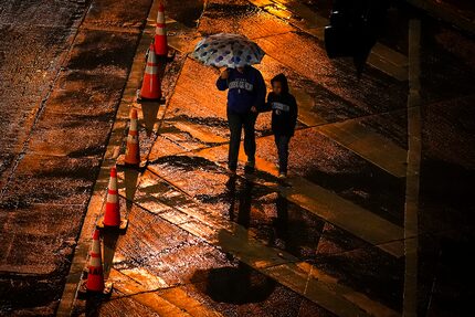 Pedestrians walk in a cold rain while crossing Dirk Nowitzki Way on Thursday, Feb. 2, 2023,...