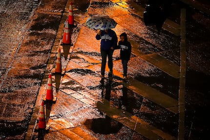 Pedestrians walk in a cold rain while crossing Dirk Nowitzki Way on Thursday, Feb. 2, 2023,...