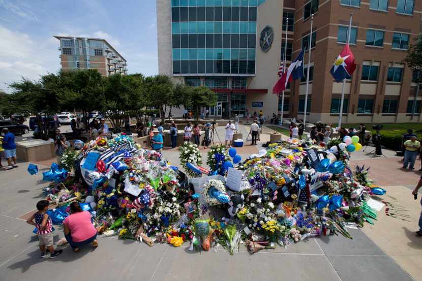 Two Dallas police cars are buried so deep in flowers and memorials that they can no longer...