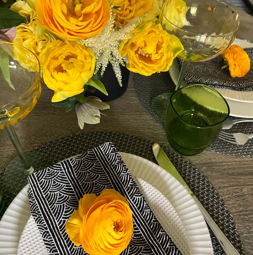 A yellow flower atop a black and white napkin on a table with a yellow floral centerpiece