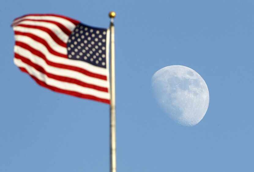 The moon rises past the U.S. flag at the Rangers Ballpark in Arlington, Saturday, July  28,...