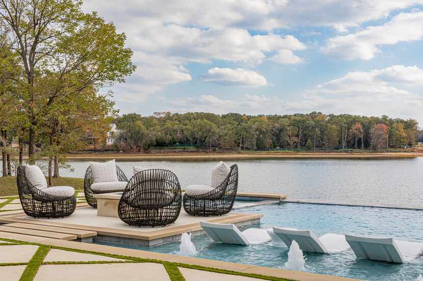 Sun-shelf pool with white loungers sits alongside a patio with black outdoor chairs arrnaged...