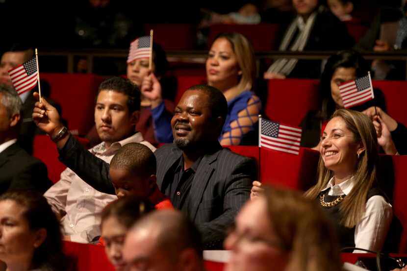 New U.S. citizen Felix Odeh, of Nigeria, (center) and other new citizens wave American flags...