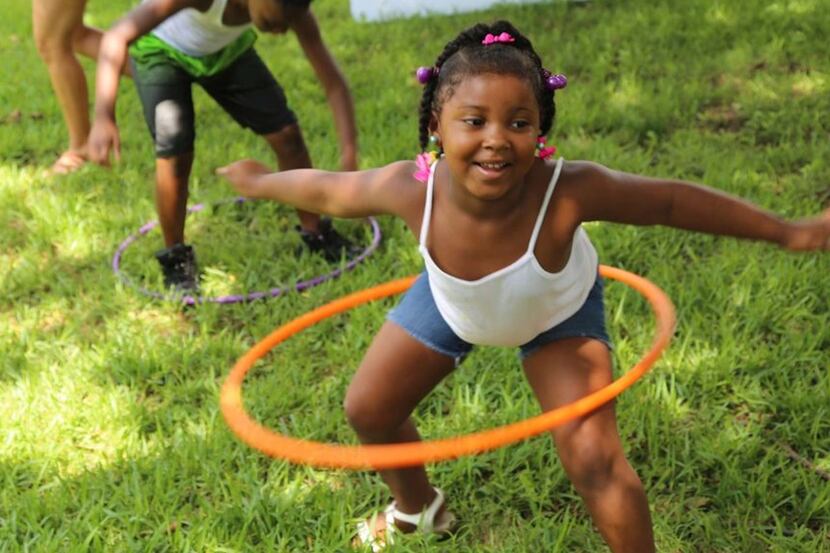 little girl with an orange hula hoop in the grass