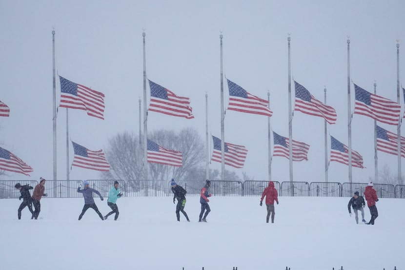 People engage in a snowball fight as U.S. flags, along the base of the Washington Monument,...