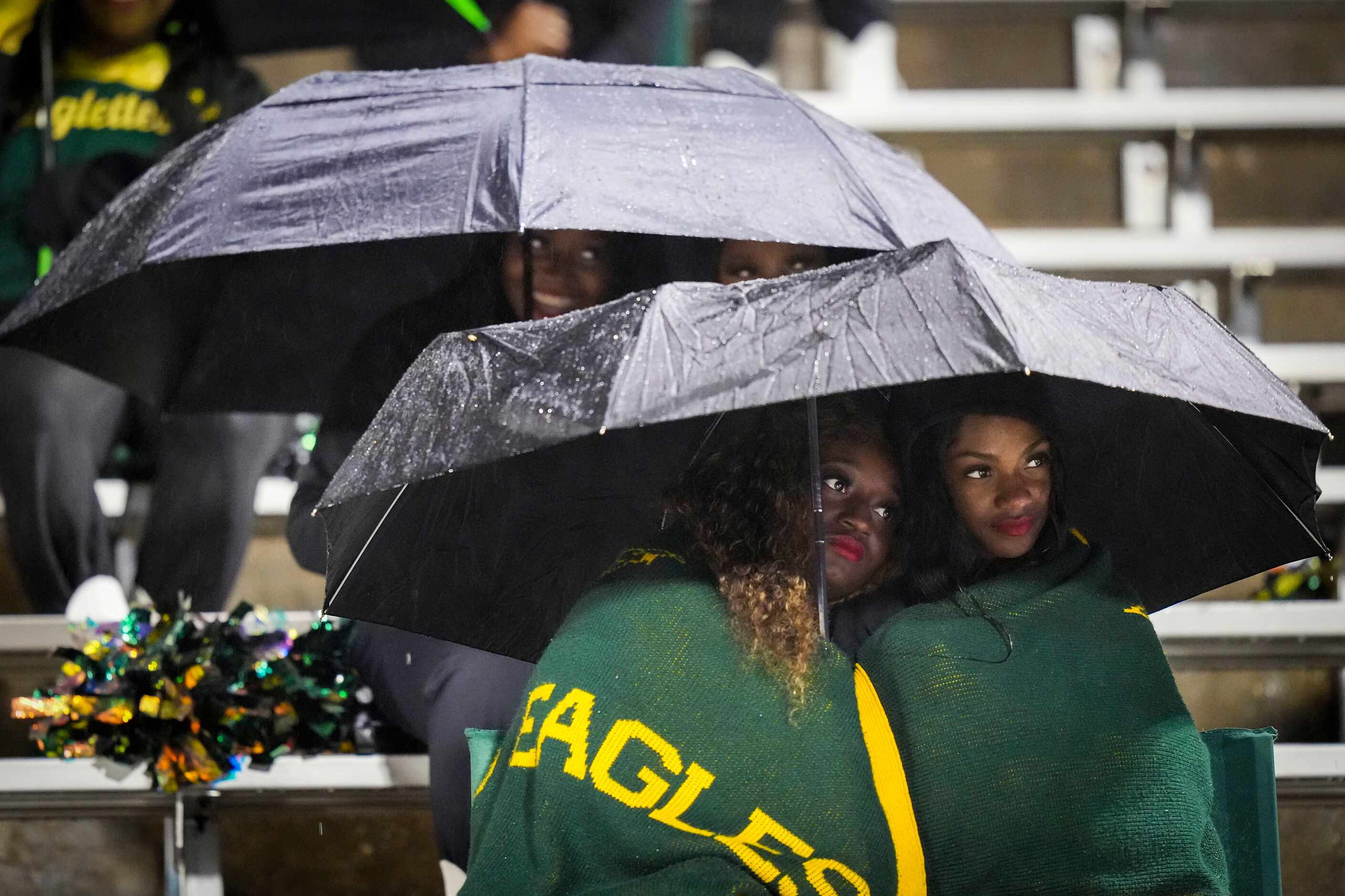 Members of the DeSoto drill team huddle under umbrellas before a District 11-6A high school...
