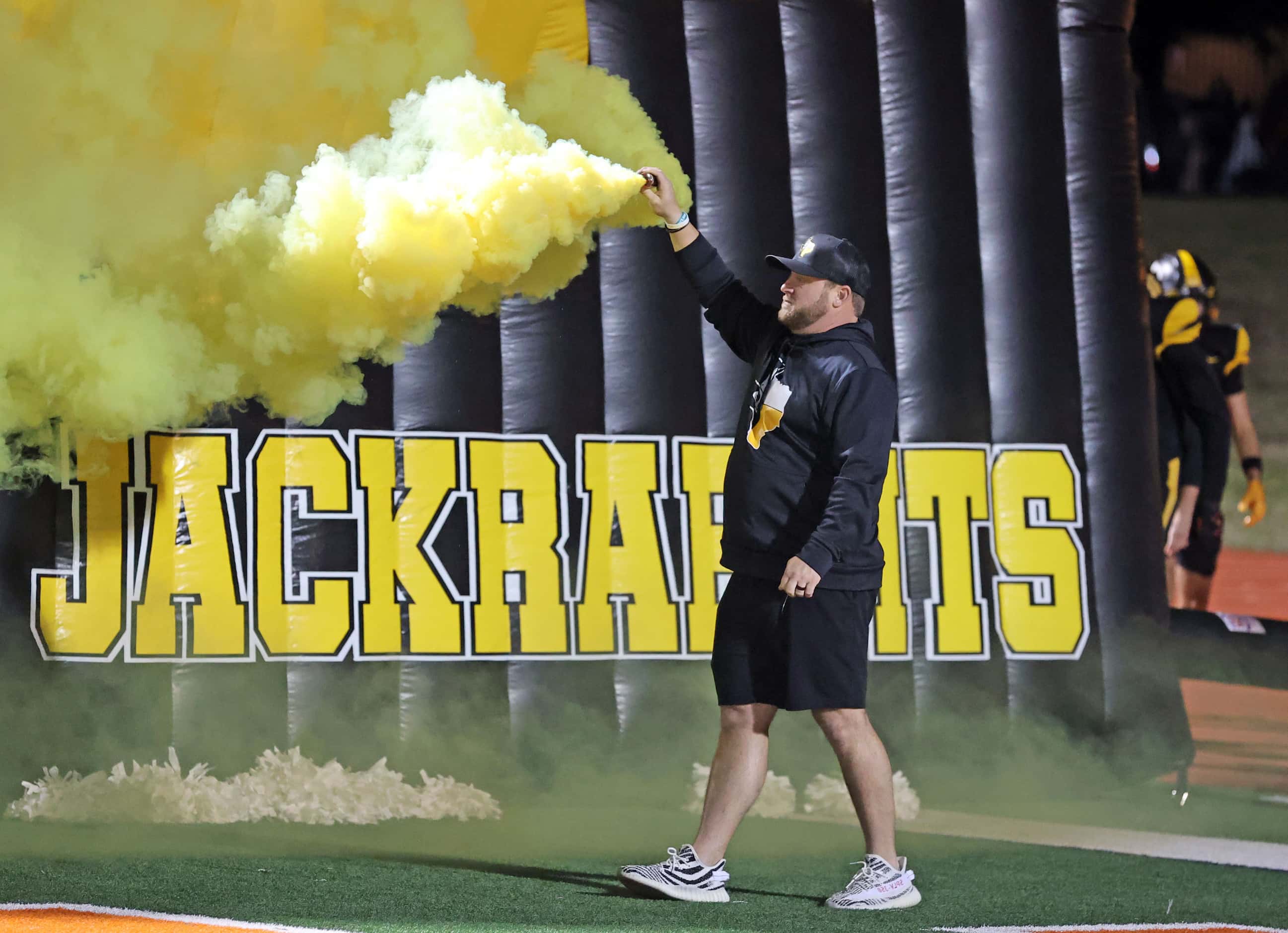 A coach holds a yellow smoke bomb, as the Forney Jackrabbits take the field during the first...