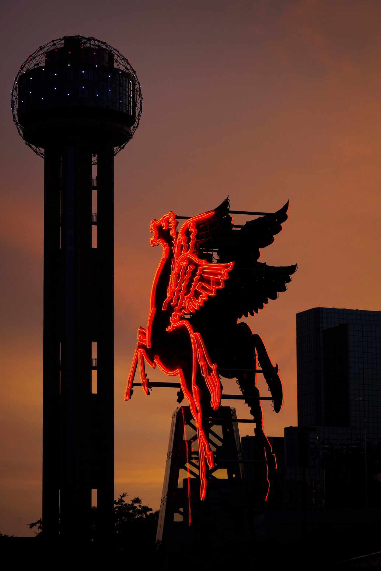 The lingering colors of sunset silhouette Reunion Tower and the neon Pegasus in front of the...