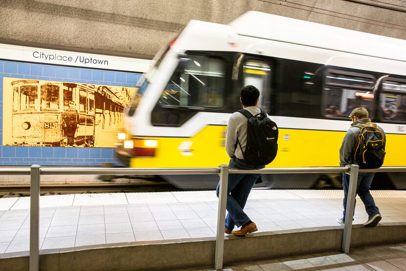 A train arrives as two men sit on a railing waiting for it to stop at the DART...