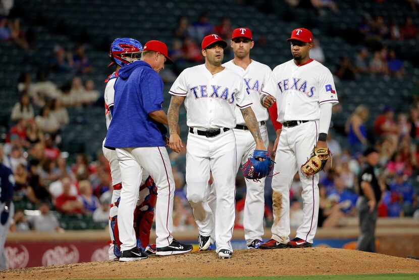 Texas Rangers relief pitcher Matt Bush center, walks off the mound after turning the ball...