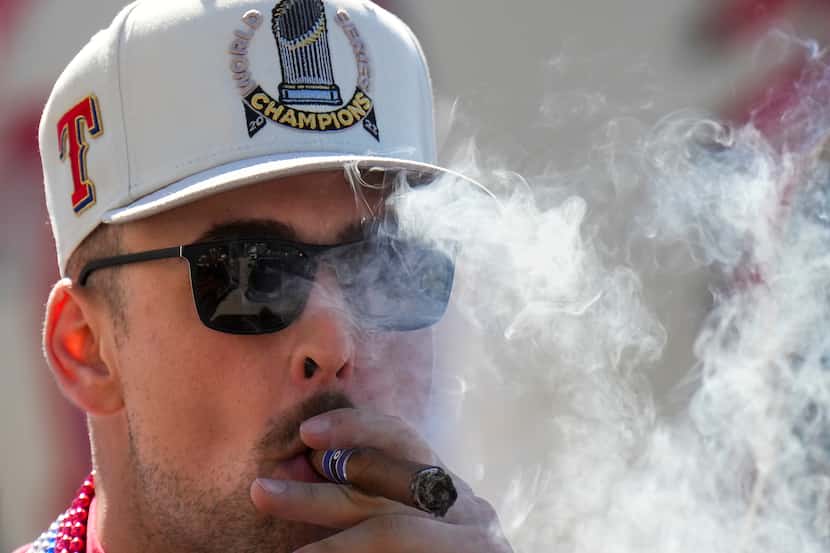 Texas Rangers first baseman Nathaniel Lowe smokes a cigar while riding a truck during a...