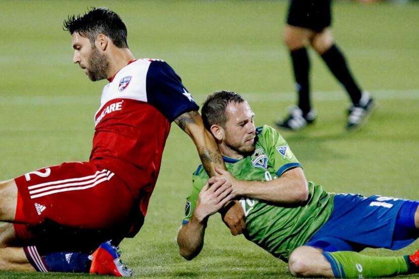 FC Dallas midfielder Ryan Hollingshead (12) is dragged to the ground by Seattle Sounders...
