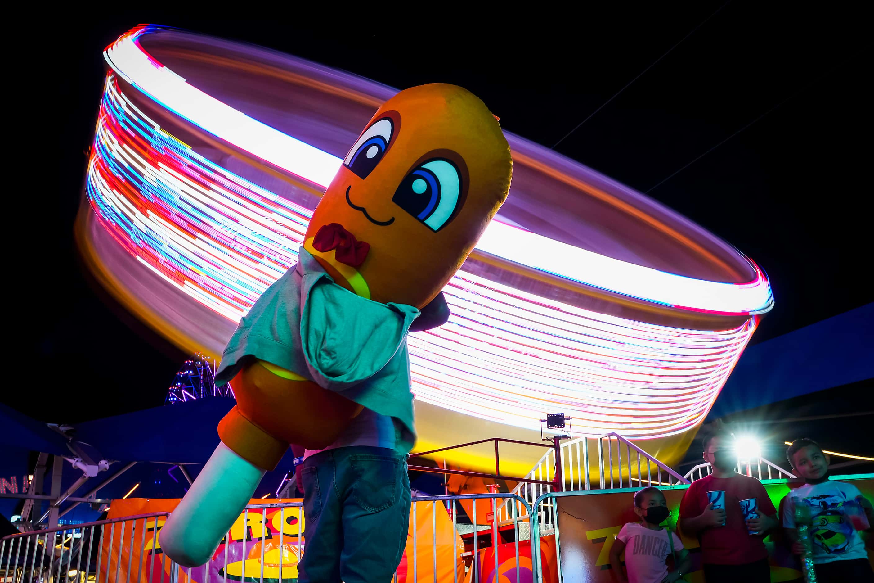 A man carries a giant stuffed corny dog as he watches the spinning Zero Gravity ride on the...