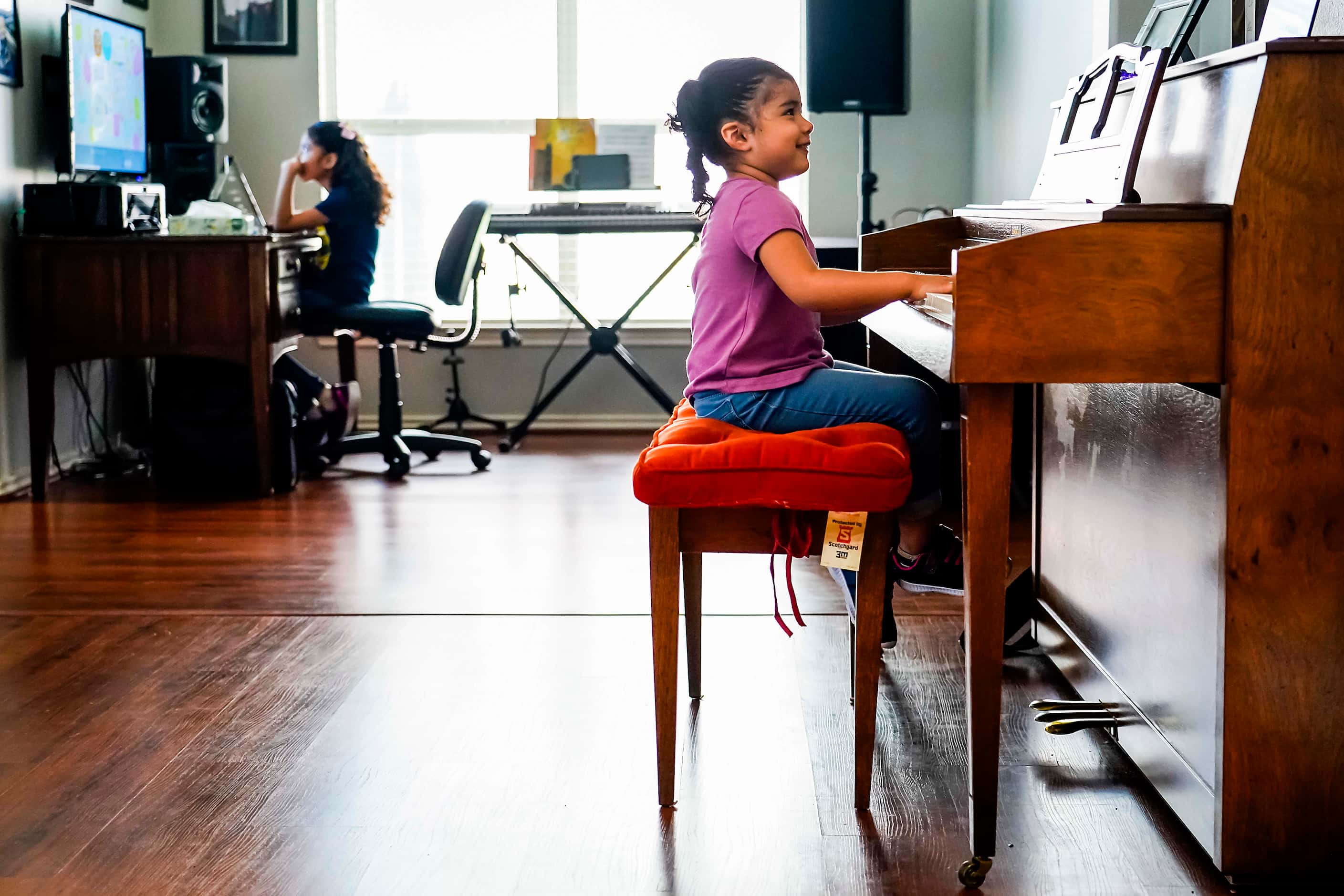 Kamila Cabrera, 4, plays the piano as her sister Selena Cabrera, 9, does school work on a...