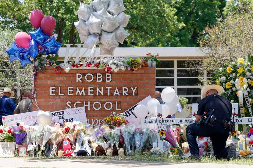 A law enforcement officer kneels as he places flowers at a memorial outside of Robb...