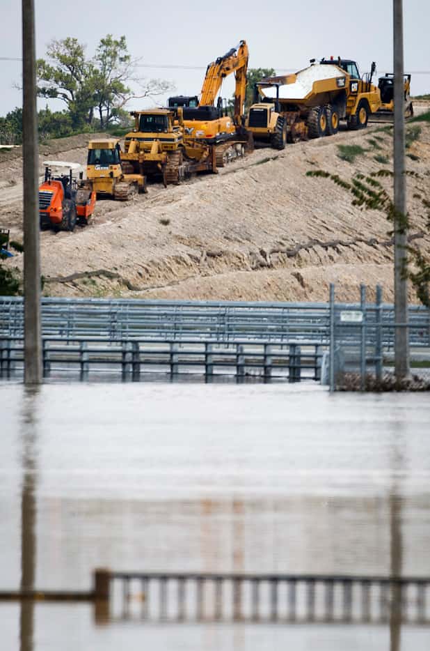 Heavy equipment is staged on an embankment leading up to the levee of the Addicks Reservoir...