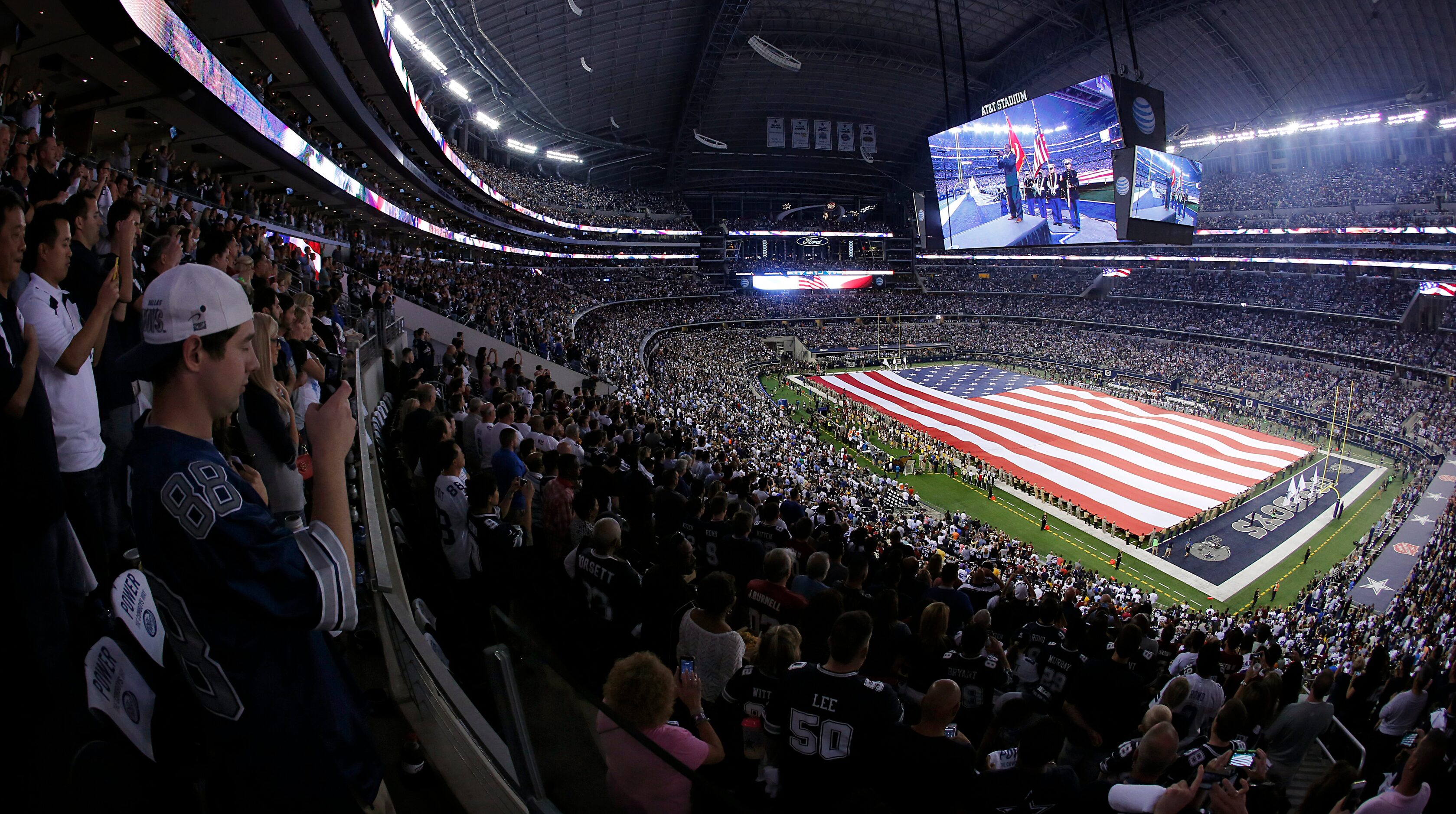 A field-sized U.S. flag is draped across the football field for the National Anthem before...