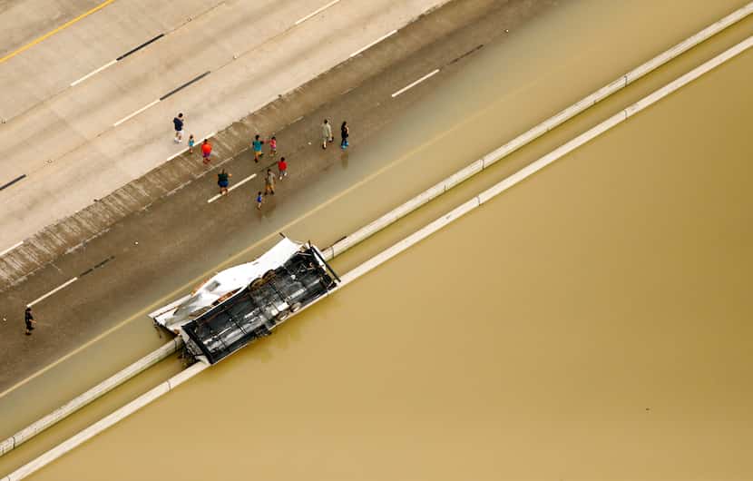 People gather along flooded Interstate 69 to see a recreational vehicle overturned in the...